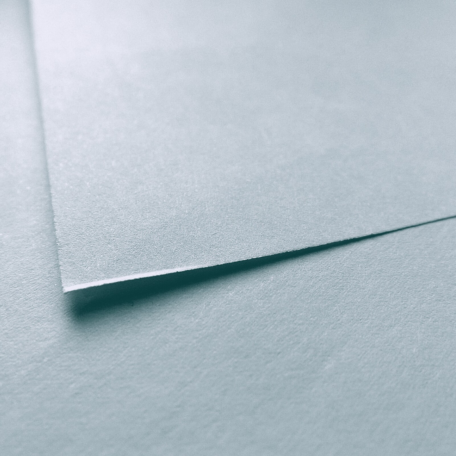 Übereinanderliegende Papierbögen in Petroltönen mit einer klaren Diagonale.