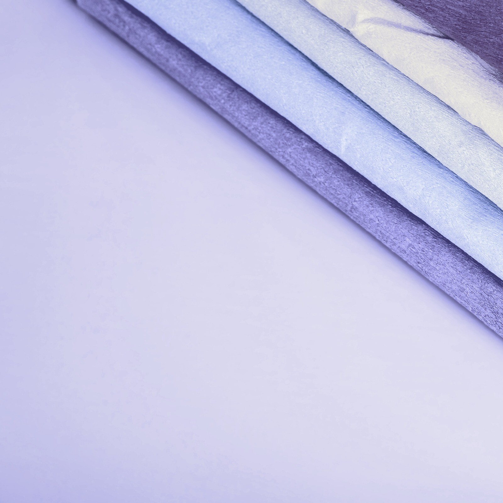Diagonal gefaltetes Textil in Lavendel- und Blautönen vor hellem Grund.